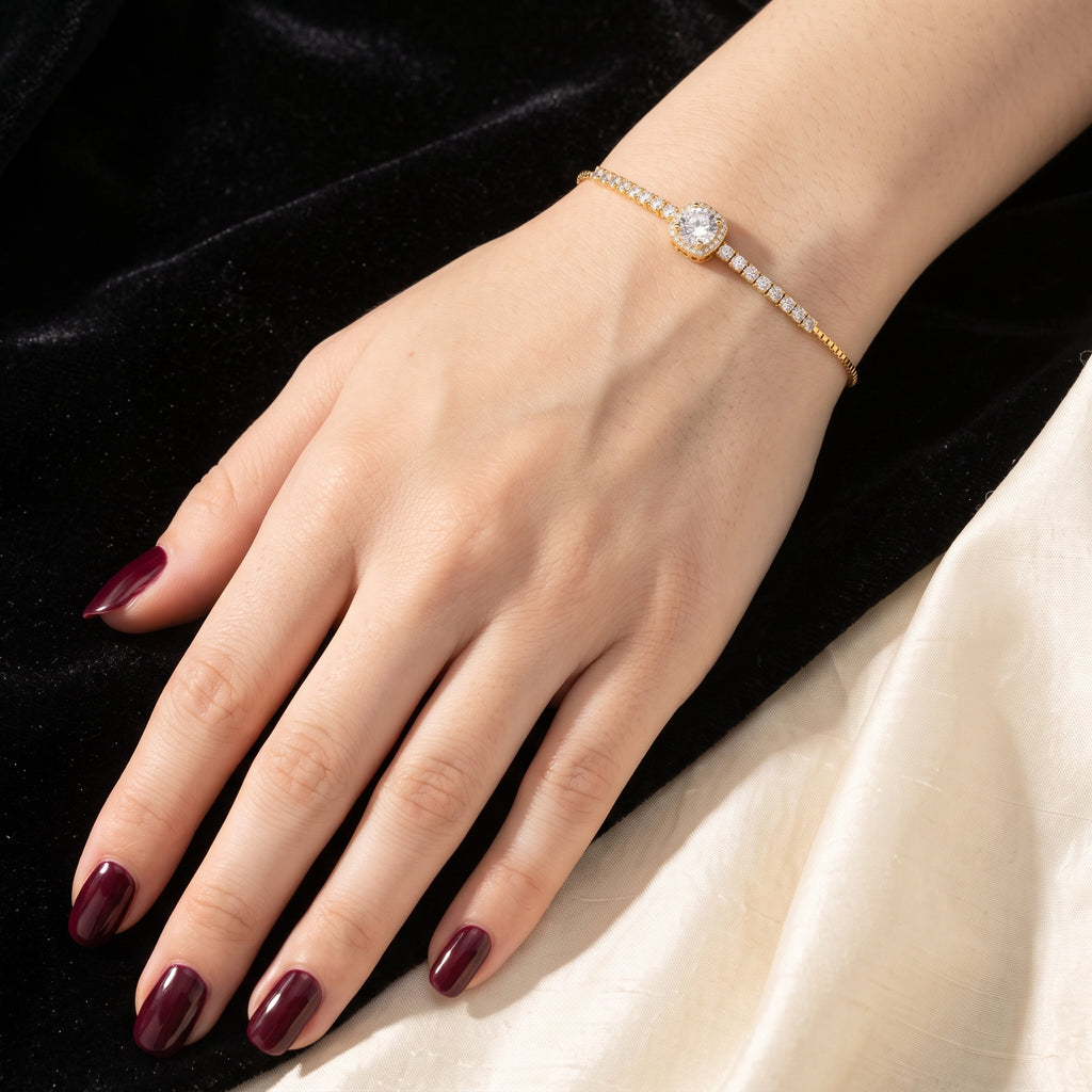 Złocona bransoletka na nadgarstku kobiety z bordowym manicure, na tle czarnego aksamitu i kremowej tkaniny