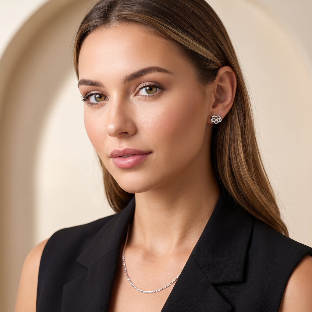 Modelka w ciemnej marynarce prezentuje srebrne kolczyki serce z cyrkoniami, kadr od ramion w górę